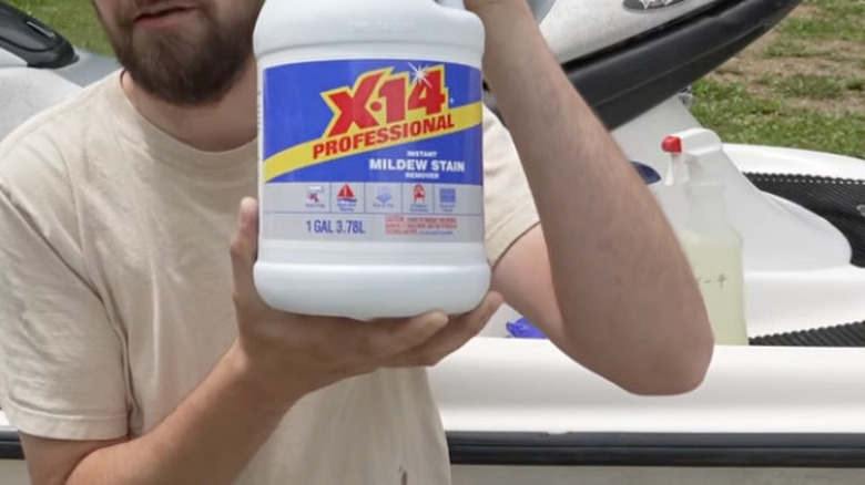 Bir adam jet skinin önünde dururken elinde bir şişe X-14 tutuyor.