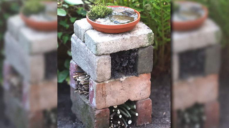Üst üste bir sulama istasyonu bulunan, üst üste dizilmiş tuğlalardan ve ince dallardan yapılmış bir DIY böcek oteli.