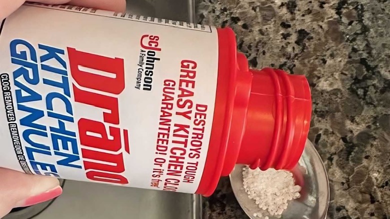 Drano Mutfak Granülleri Drenaj Tıkanıklığı Giderici ve Temizleyiciyi kaşığa ekleyen bir kişi