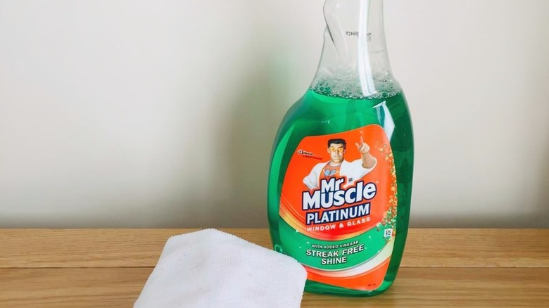 bir şişe Mr. Muscle Platinum Pencere ve Cam Temizleyici Sprey ve bir bezin yanında