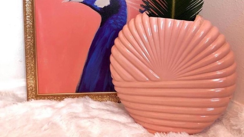 Bir tavus kuşu resminin yanında kabarık bir halının üzerine yerleştirilmiş pembe vintage Art Deco Revival vazo.