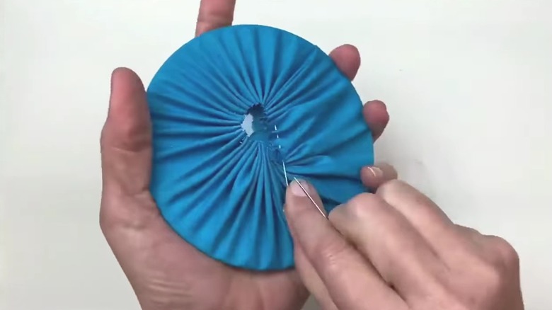 Eller bir CD'nin etrafına mavi kumaş dikiyor.