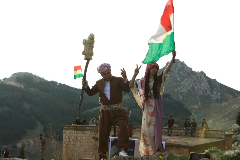 Ellerinde Kürt bayrakları olan Iraklı Kürtler, koronavirüs hastalığının (COVID-19) yayılmasının ortasında, Irak Kürdistanı'nın Duhok yakınlarındaki Akra kasabasında baharın ve yeni yılın ilk gününü kutlayan bir festival olan Nevruz Günü'nü kutluyor