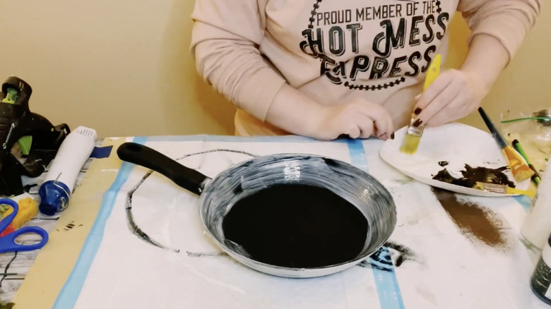 Bir kadın eski bir tavayı siyah beyaz boyayla boyuyor.