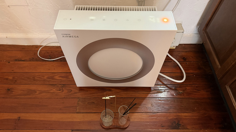 Önünde yerde bir tütsü bulunan ve kırmızı hava kalitesi göstergesi bulunan Airmega Mighty2
