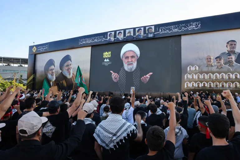 Lübnan Şii hareketi Hizbullah'ın destekçileri, eski lider Hasan Nasrallah'ın 27 Eylül 2026'da Beyrut'un güney banliyölerinde İsrail tarafından düzenlenen bir saldırıda öldürülmesinin ikinci yıldönümü münasebetiyle düzenlenen tören sırasında Hizbullah şefi Naim Kasım'ın televizyonda yayınlanan konuşmasını izlerken sloganlar atıyorlar.