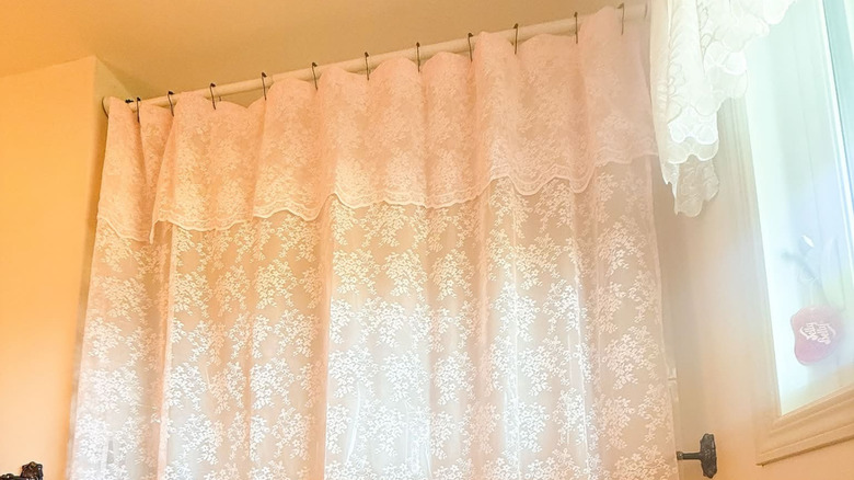 Saçaklı beyaz dantelli bir duş perdesi banyodaki bir çubuktan sarkıyor.