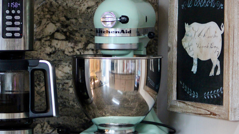 Tezgahın üzerinde cezvenin yanında metal bir kase bulunan deniz mavisi KitchenAid