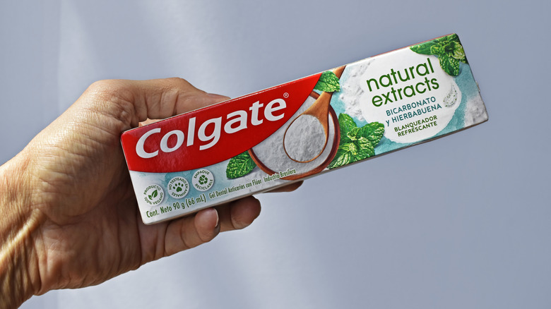 Bir kutu Colgate doğal özleri diş macunu tutan bir kişi