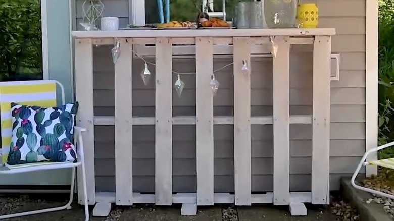Taş verandada büfe istasyonu olarak kullanılan, ahşap paletlerden yapılmış beyaz bir bar tezgahı.