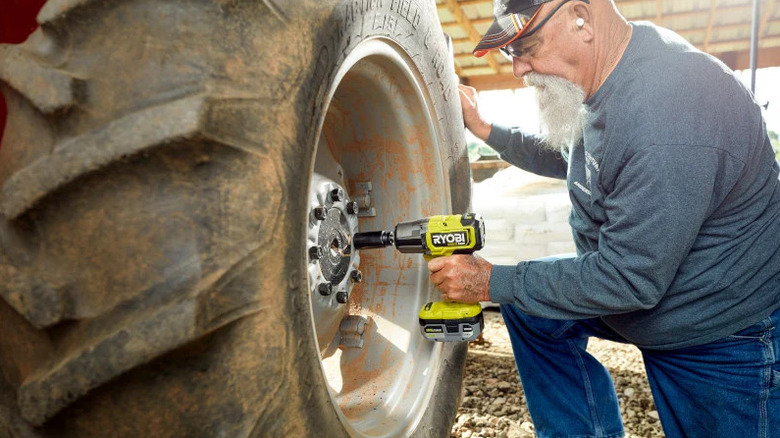 Traktör lastiğindeki bijonları çıkarmak için Ryobi ONE+ 18V Darbeli Anahtarı kullanan bir adam
