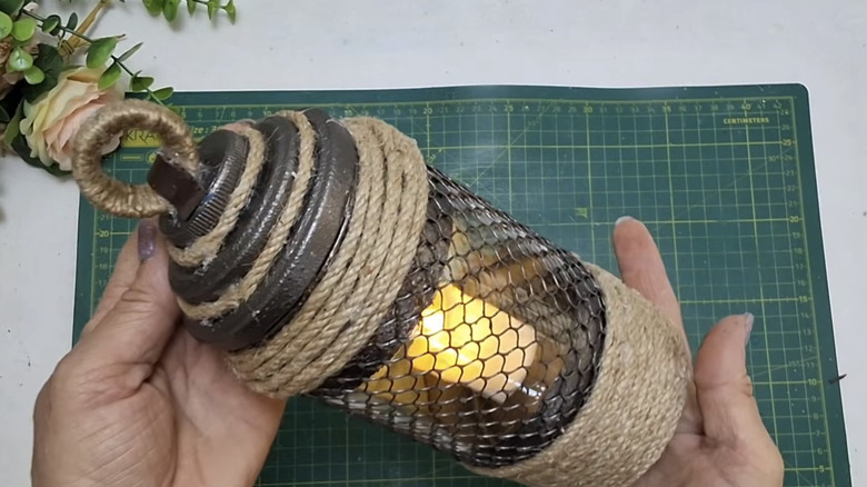 Elinde cam kavanoz, ton balığı konservesi, ip ve diğer el işi malzemelerinden yapılmış bitmiş bir DIY fener tutan kişi