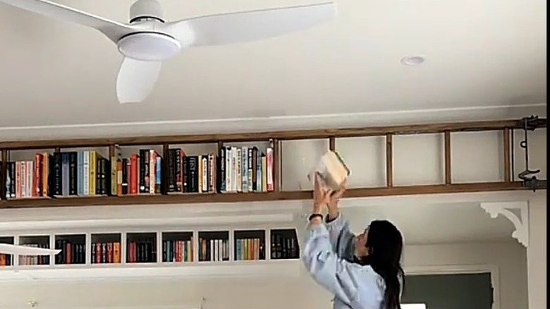 Bir kadın kitapları duvara yatay olarak asılan bir merdivene yerleştirir.
